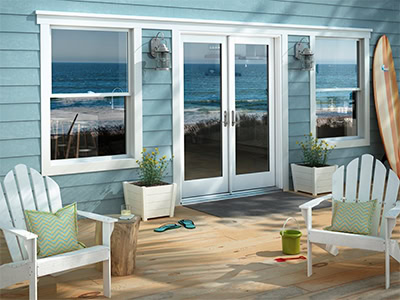 A beachside patio in FL with two white Adirondack chairs, a small table, potted plants, and scattered beach items faces glass doors—expert glass repair Pinellas County ensures clear views of the ocean and shoreline beyond.