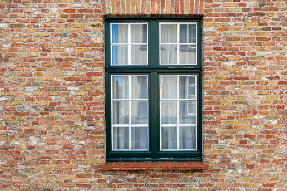 High-quality green-framed double-hung window with glass panes on a brick building, showcasing expert glass replacement services.